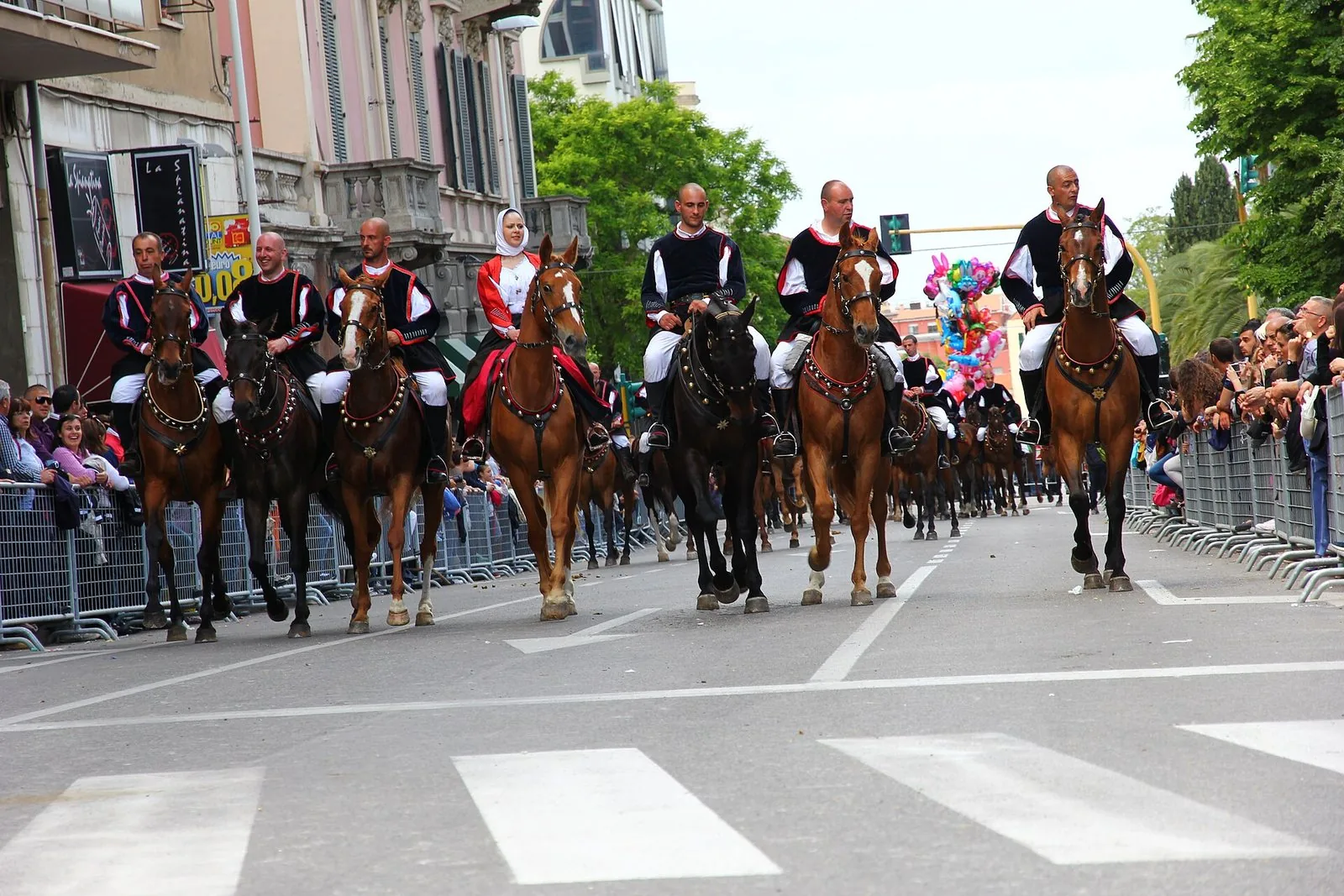 Cavalieri in abito tradizionale sardo sfilano a cavallo lungo una strada di Sassari durante la Cavalcata Sarda, con il pubblico dietro le transenne ai lati