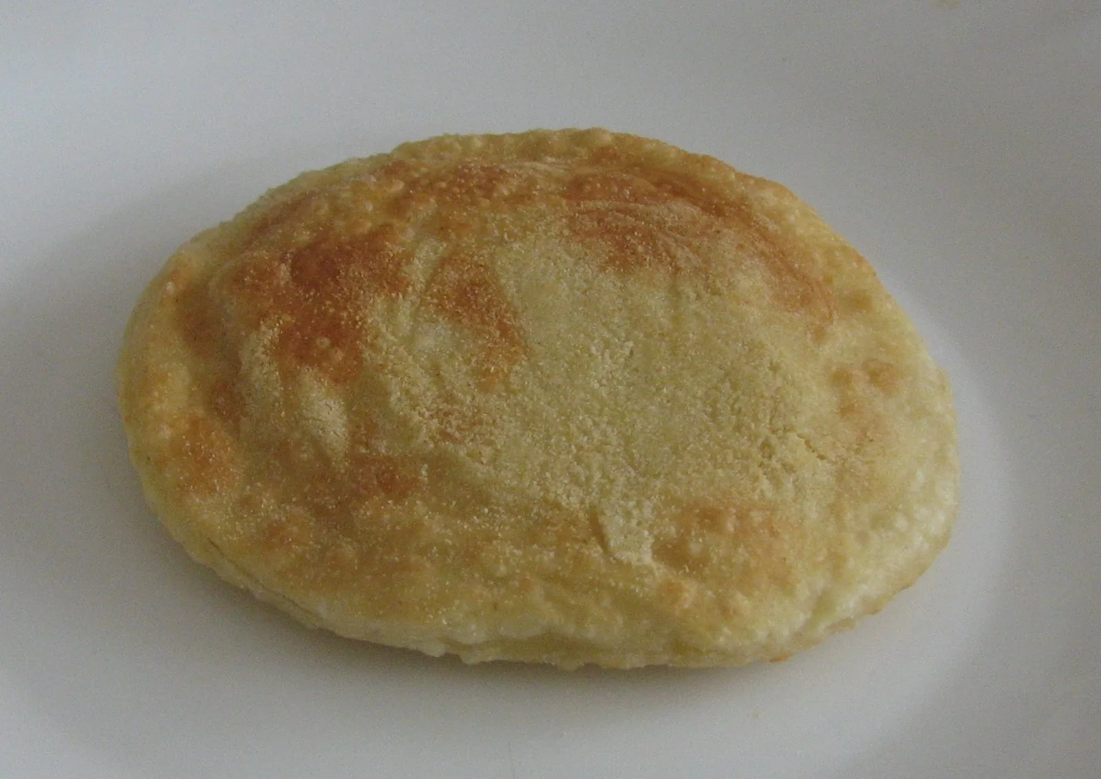 Una seada fritta, disco di pasta dorata ripieno di formaggio, su un piatto bianco in attesa del miele